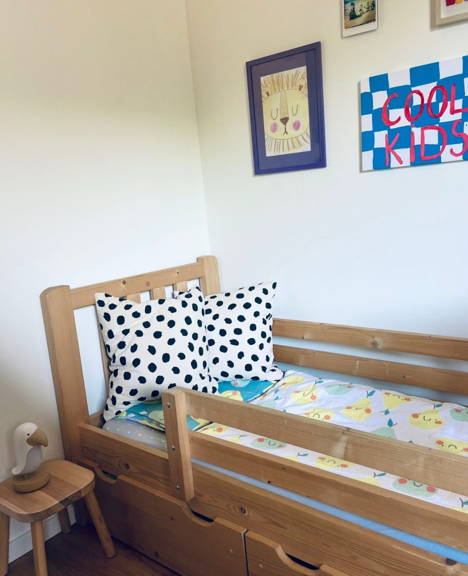 Holzbett für Kinder mit gepunkteten Kissen und buntem Bettlaken in einem hellen Zimmer.