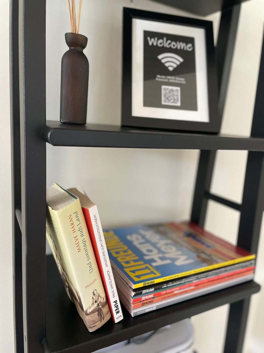 Regal mit Büchern, dekorativer Vase und einem Rahmen mit WLAN-QR-Code.