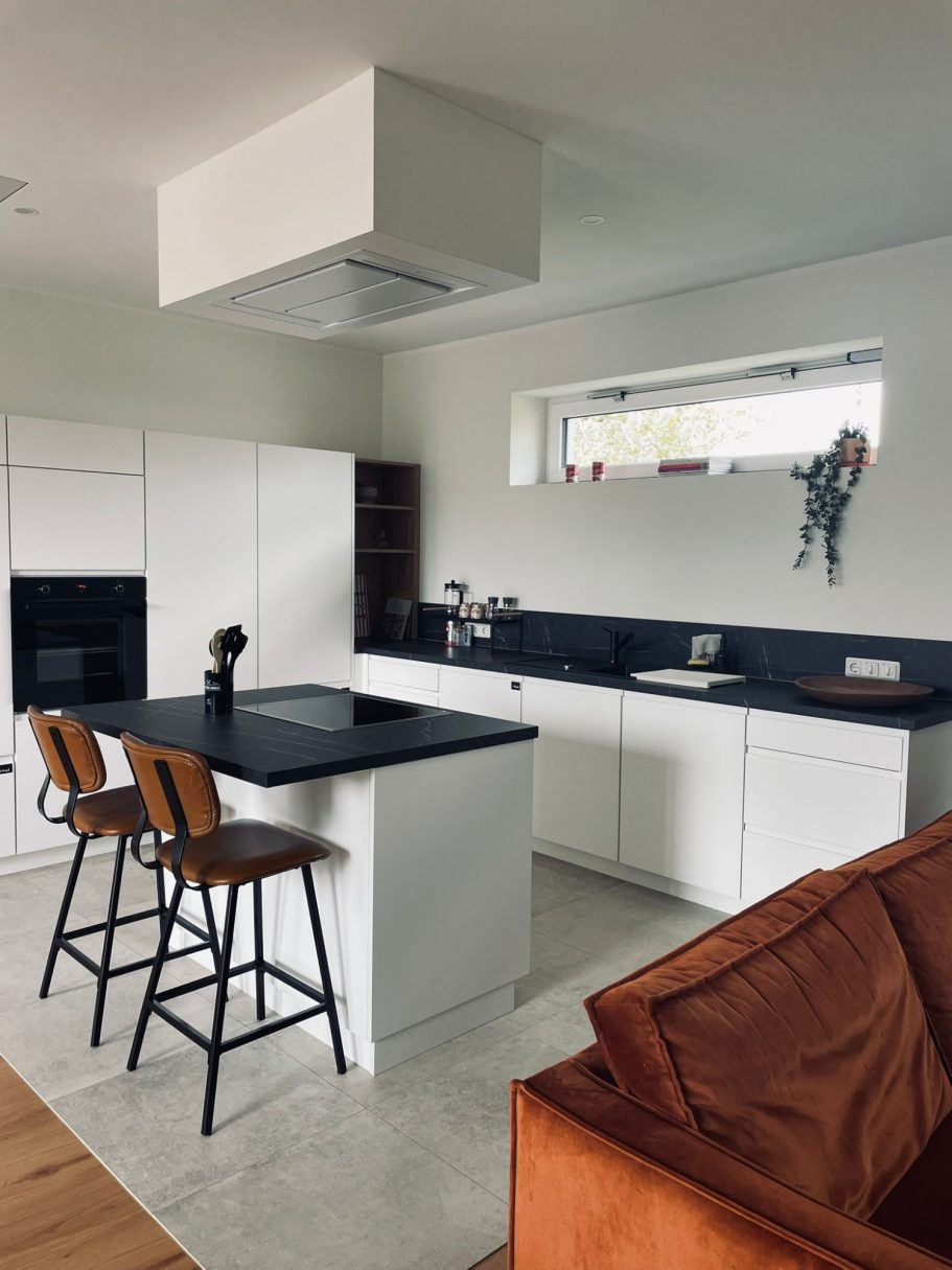 Moderne Küche mit weißen Schränken, schwarzem Tisch und Holzstuhl. Heller Raum mit Fenster.