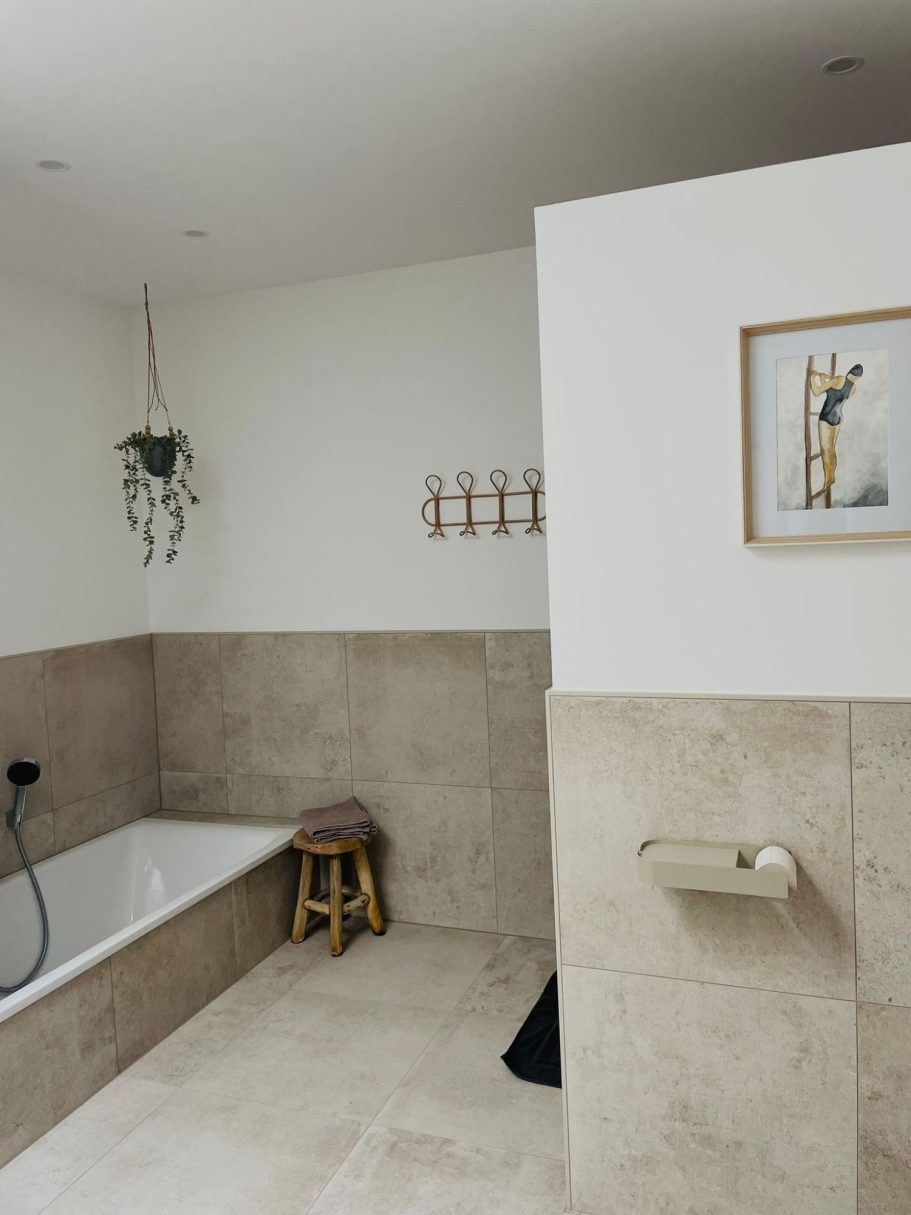 Modernes Badezimmer mit Badewanne, Hocker und dekorativen Pflanzen.